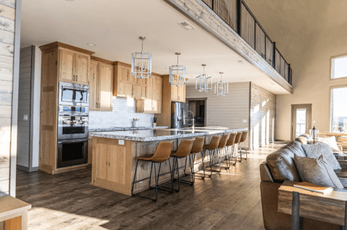 Modern kitchen with wooden cabinets, a large island, and bar stools, featuring open space and natural light.